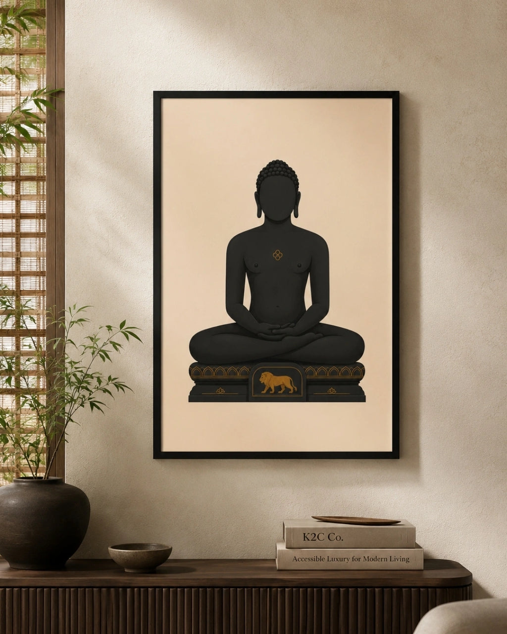 A framed wall art print featuring a seated Mahavira silhouette in black on a warm beige background, hung above a dark wooden console table with books and a plant in a styled interior.
