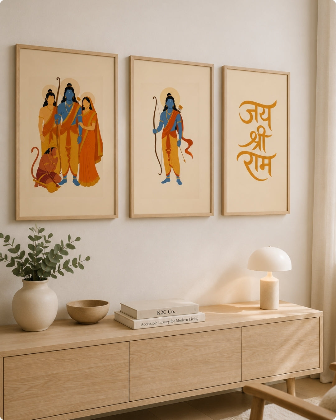 Three framed art prints with a warm neutral aesthetic are displayed on a wall above a light wood console table. The prints feature stylized illustrations of Hindu deities in orange, blue, and yellow tones, alongside golden Devanagari script.