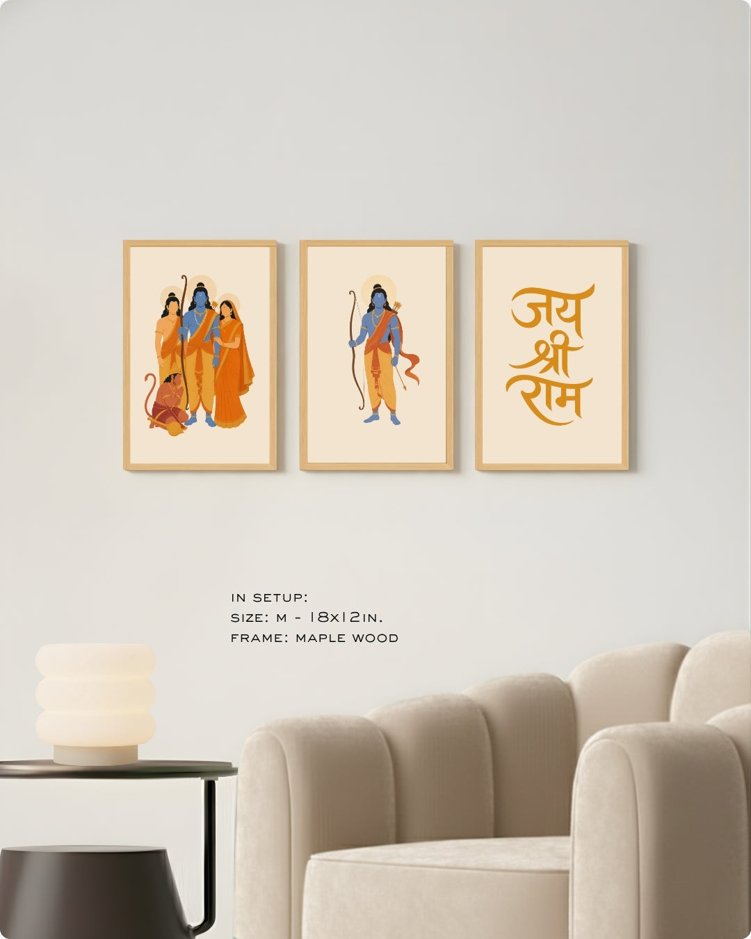 Three framed wall art prints displayed above a beige armchair in a living room setting. The prints feature stylized illustrations of the Holy Family in orange and blue garments, and the Sanskrit mantra 'Jai Shree Ram' in orange.