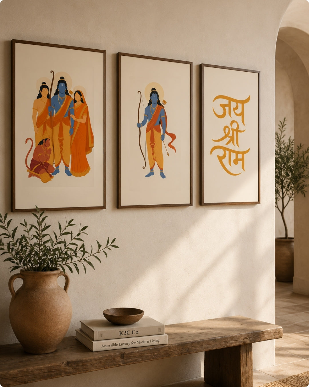 Three framed wall art prints hang above a wooden bench in a warm, sunlit room. The left two frames show stylized depictions of Lord Ram and the monkey, and the right frame has orange Devanagari text on a cream background.