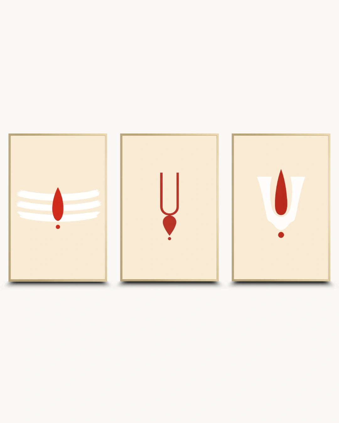 Three modern minimalist framed wall art prints with gold-toned frames on a light gray background. Each print features a red spiritual symbol on a warm cream background: a white and red Shiva trident on the left, a red pendant on the center, and a white and red symbol on the right.