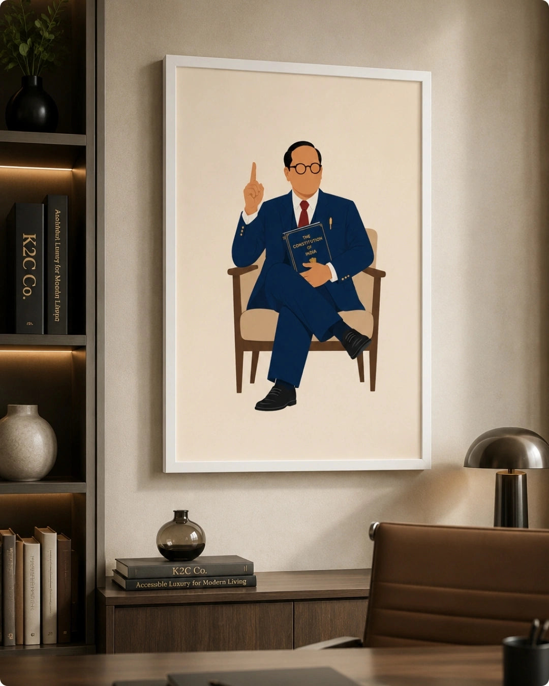 A framed art print featuring a stylized illustration of Dr. B.R. Ambedkar in a blue suit sitting in an armchair, displayed on a beige wall in a modern home office setting.
