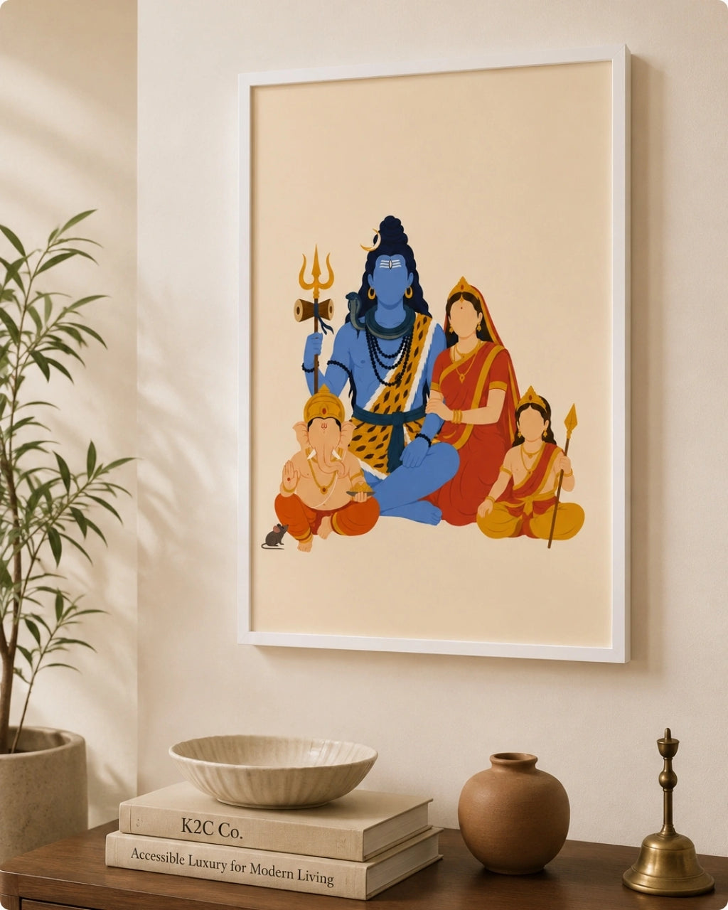 A framed art print featuring stylized illustrations of Hindu deities, displayed on a beige wall above a wooden console table with books, a bowl, a vase, and a brass bell.