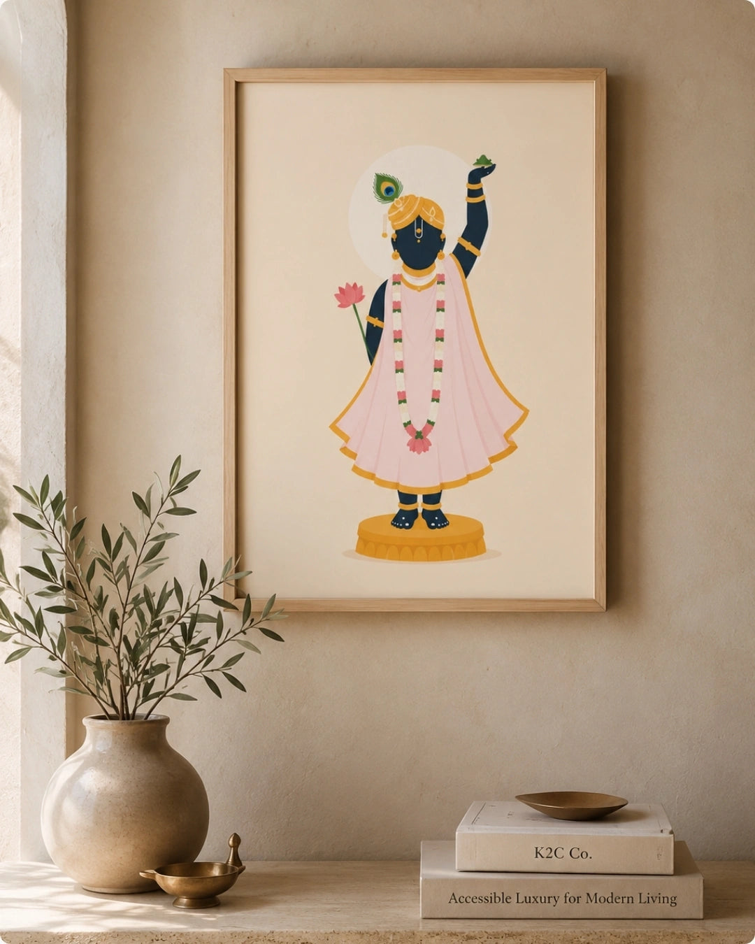 A framed art print featuring a stylized illustration of the Hindu deity Shrinathji in a pink dhoti and yellow crown, displayed on a beige wall above a shelf with a vase and books.