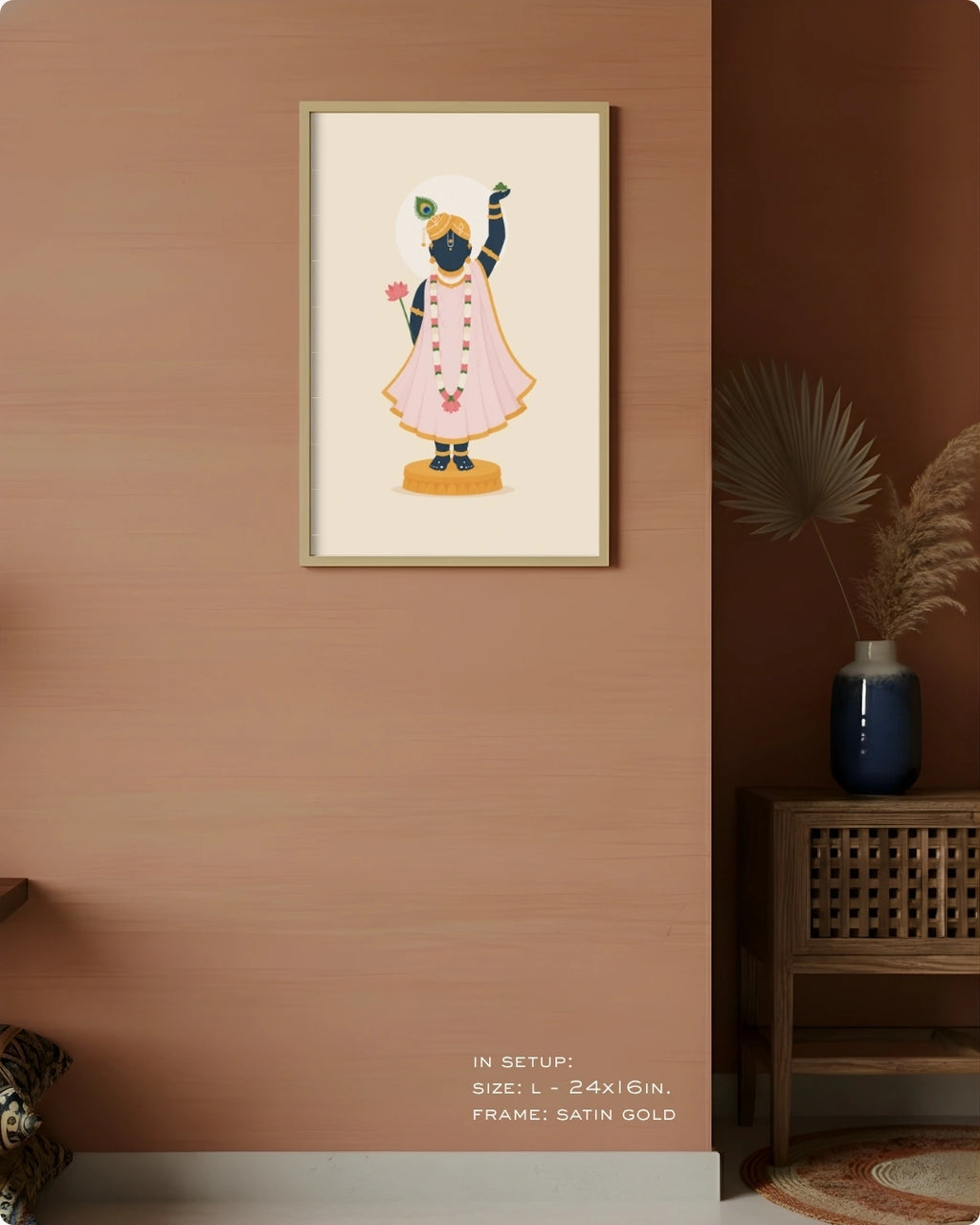 A framed art print of lord Shrinathji in a pink robe, displayed on a warm terracotta wall in a styled room setting with a wooden side table and vase.