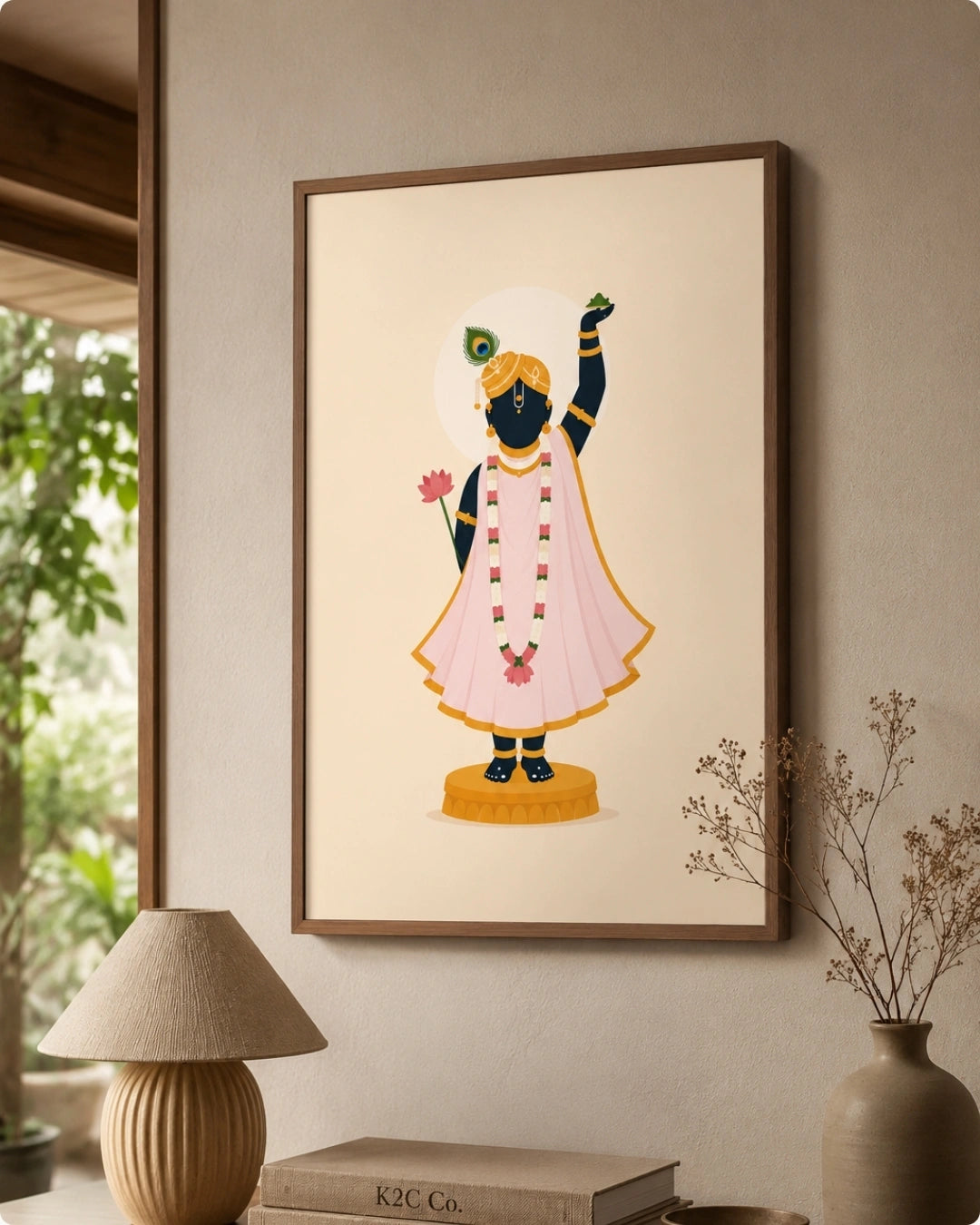 A framed art print of the Hindu deity Shrinathji, styled on a beige wall above a table with a lamp, books, and a vase.
