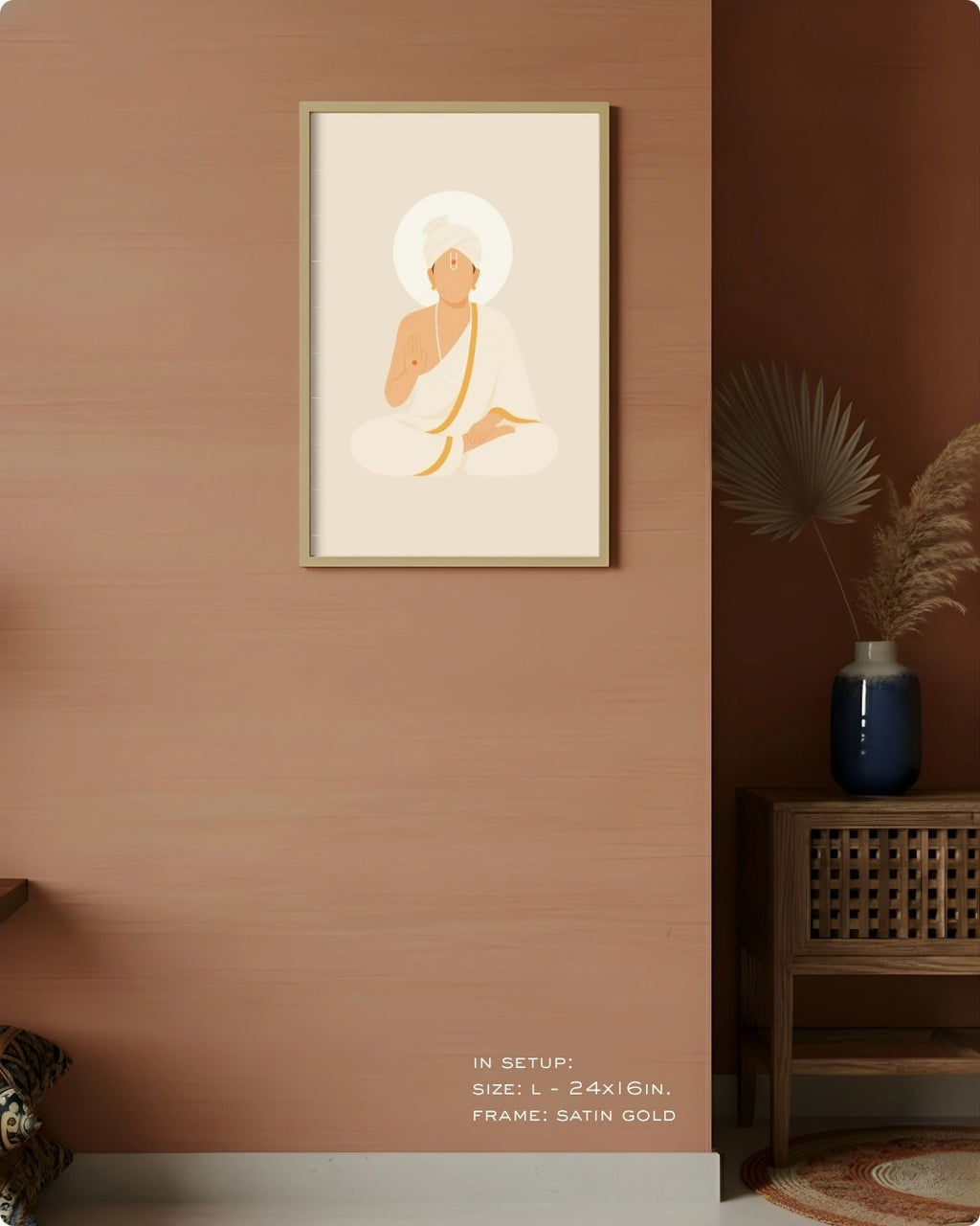A framed minimalist art print of Swaminarayan with a halo, displayed on a warm terracotta wall in a styled interior setting with a wooden side table, blue vase, and dried palm leaves.