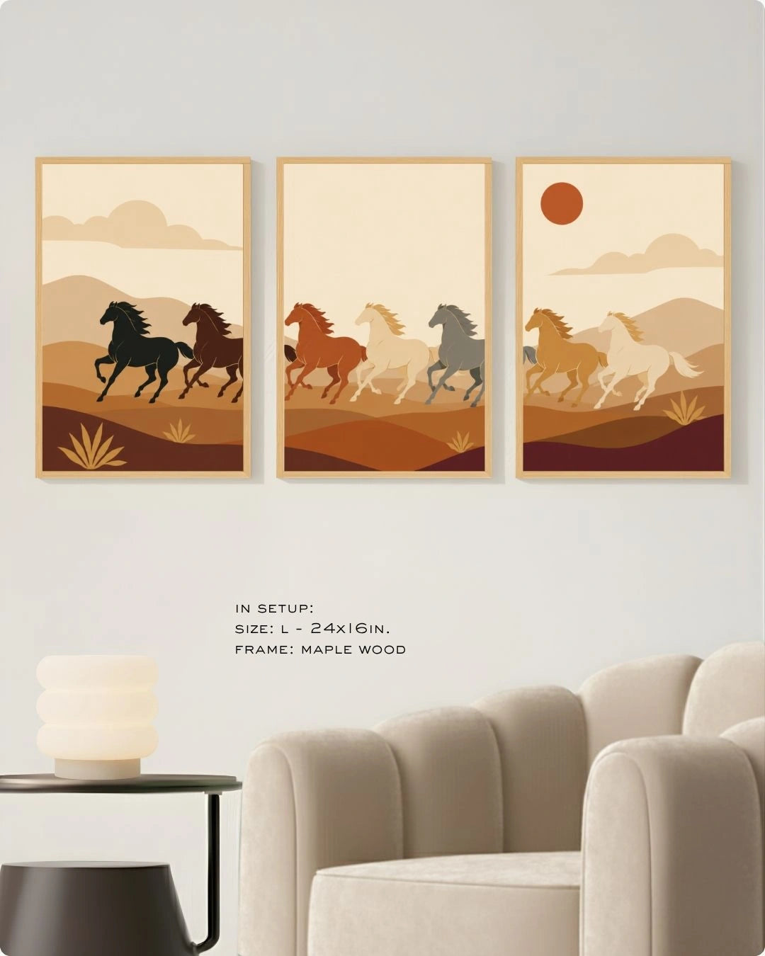 A set of three large maple wood-framed wall art prints hanging above a plush cream velvet armchair in a modern minimalist lounge. The triptych features stylized horses running through an earth-toned desert landscape. Text on the wall indicates the size is L - 24x16 inches. A sleek black side table with a contemporary stacked frosted glass lamp sits next to the chair.