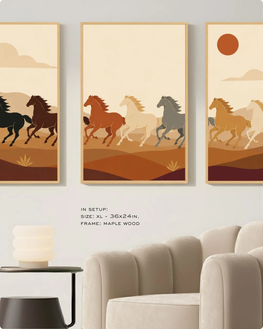 A set of three extra-large maple wood-framed wall art prints hanging above a plush cream velvet armchair in a modern minimalist lounge. The triptych features stylized horses running through an earth-toned desert landscape. Text on the wall indicates the size is XL - 36x24 inches. A sleek black side table with a contemporary stacked frosted glass lamp sits next to the chair.