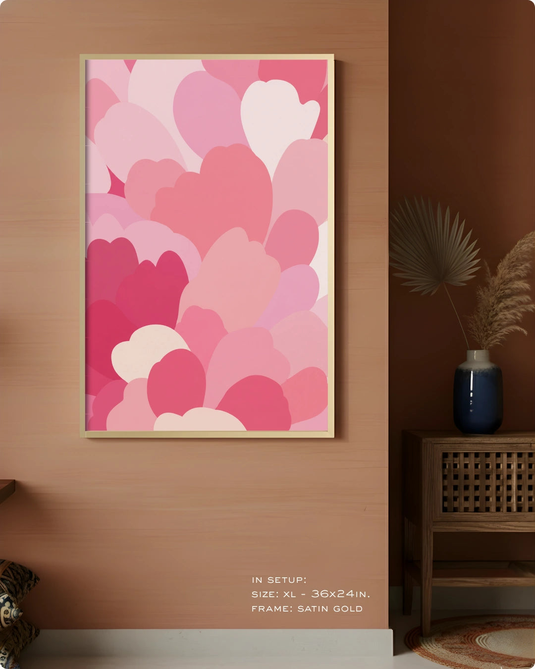 A framed wall art print featuring overlapping abstract hearts in pink, magenta, and white, displayed on a warm wood wall in a styled interior setting with a side table and vase.
