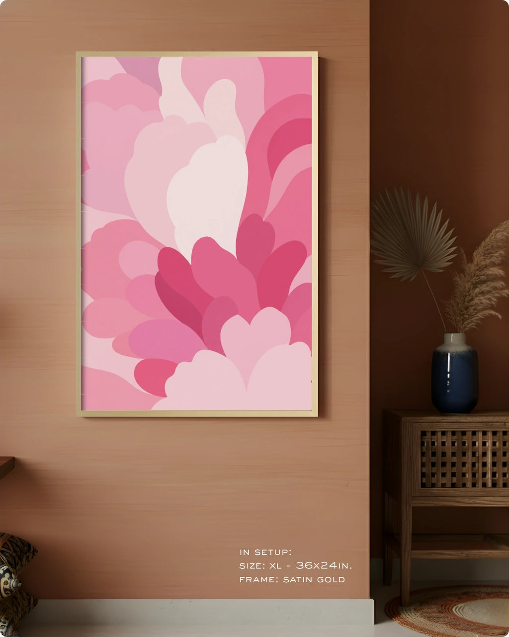 A framed abstract floral art print with layered pink and magenta petal-like shapes hangs on a warm wood wall in a styled interior. The frame is satin gold.