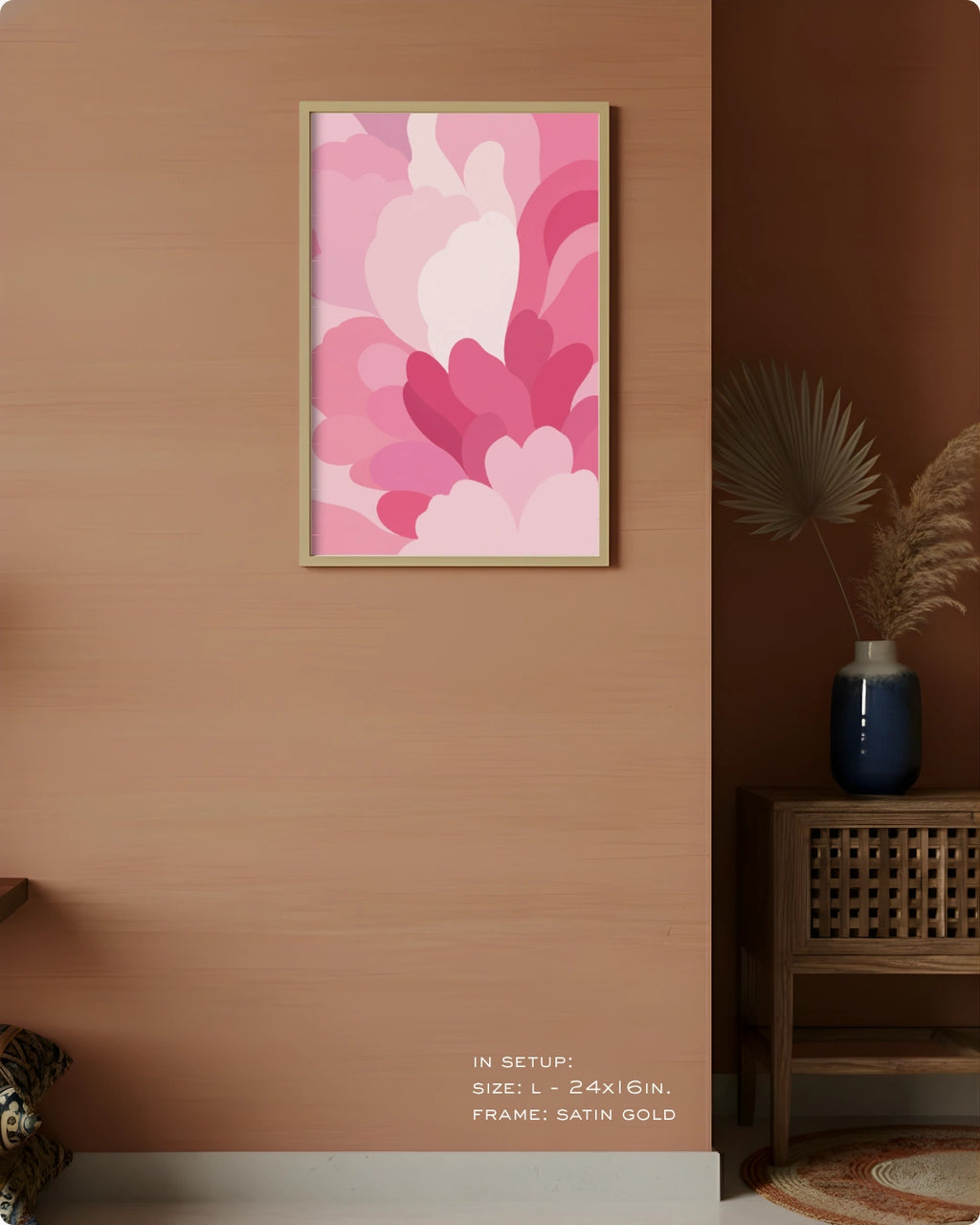 A framed abstract floral wall art print in pink tones hangs on a warm peach wall in a styled interior setting. The artwork features layered petal-like shapes in shades of pink, magenta, and light blush.