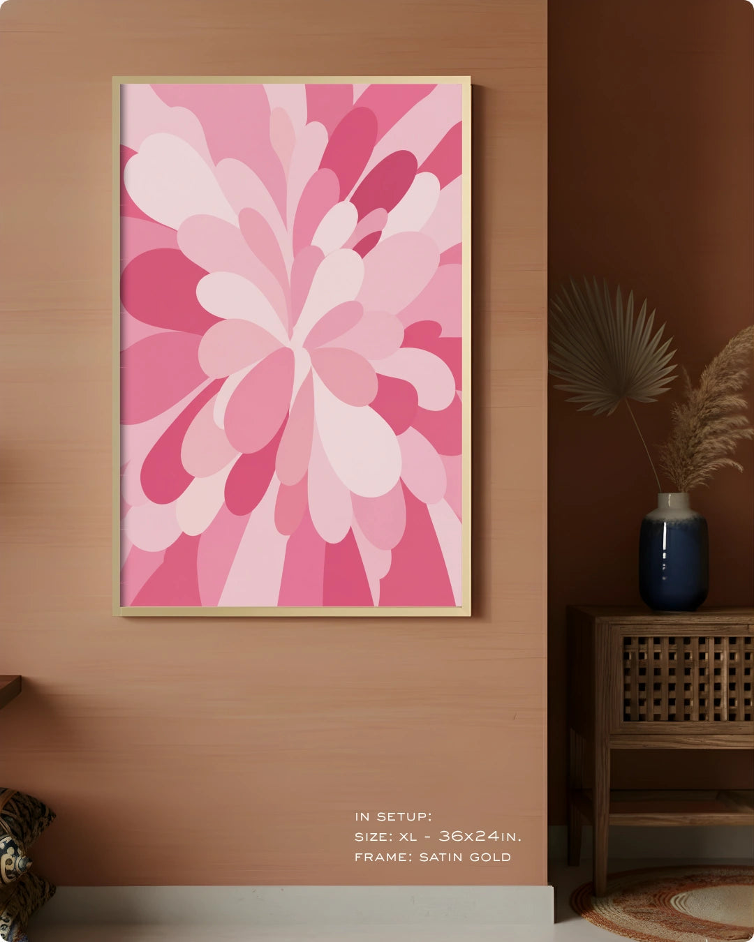 A framed abstract floral wall art print in shades of pink and white, displayed on a warm brown wall in a styled interior setting with a side table and vase.