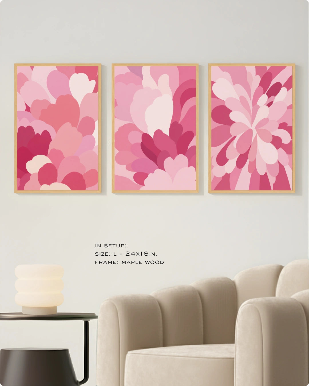 Three framed abstract floral wall art prints in shades of pink and magenta hang on a light wall above a beige armchair, with small text noting the size and maple wood frame.