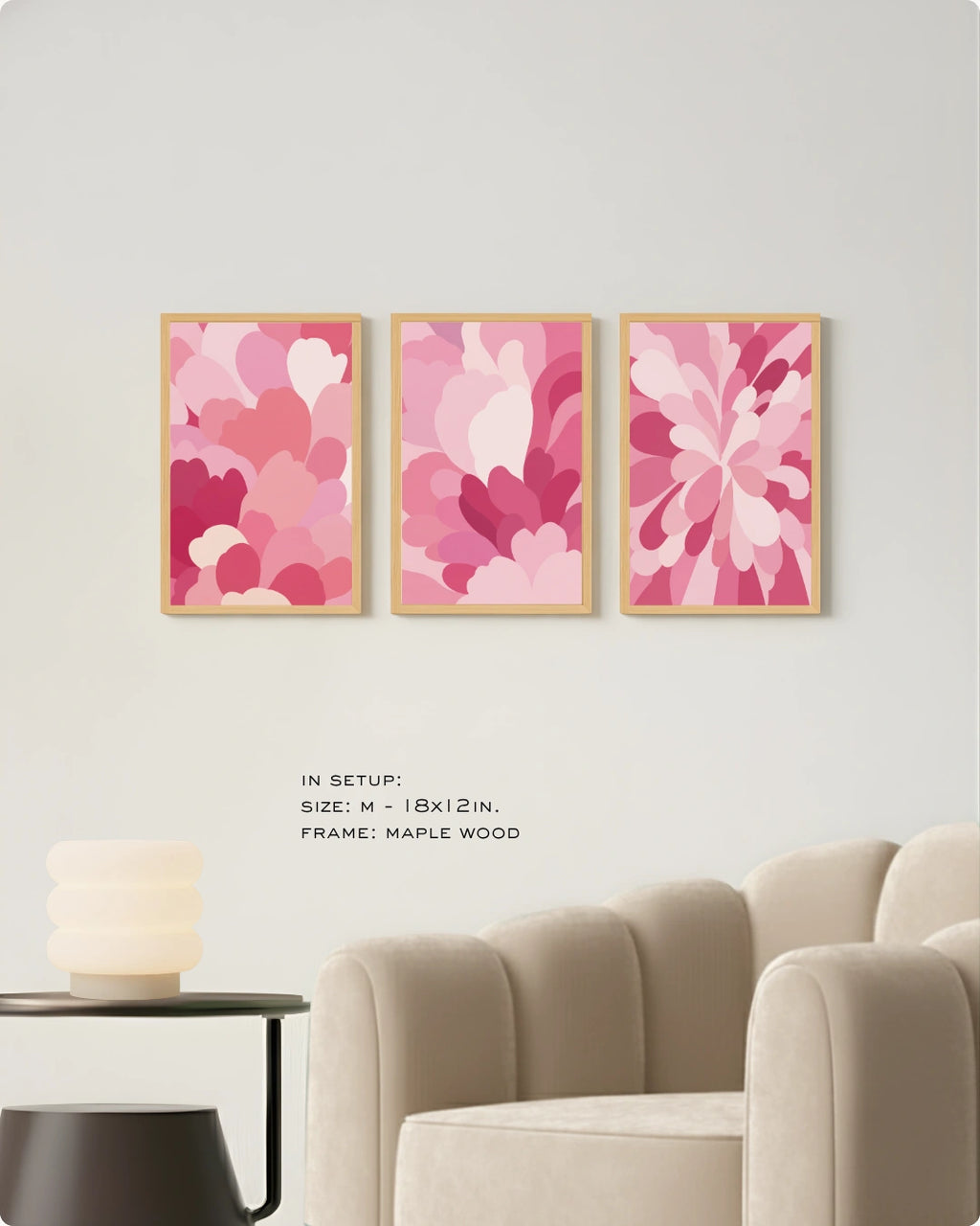 Three framed abstract floral wall art prints in shades of pink and magenta hang on a light gray wall above a beige armchair, with small text noting size and maple wood frame.