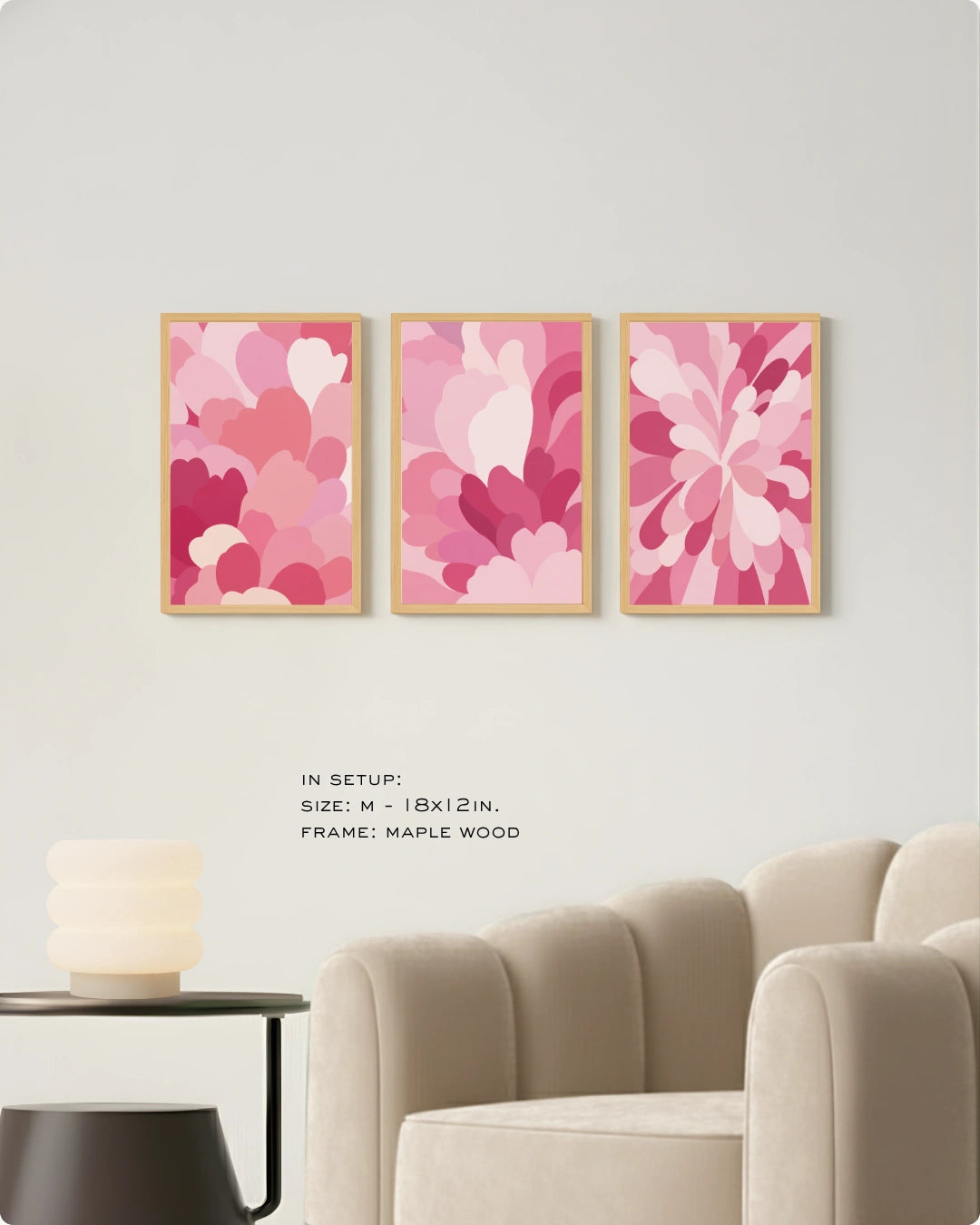 Three framed abstract floral wall art prints in shades of pink and magenta hang on a light gray wall above a beige armchair, with small text noting size and maple wood frame.