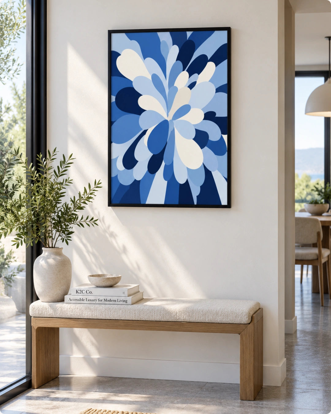 A framed abstract floral art print in shades of blue and white hangs on a beige wall above a wooden bench with a cushion in a bright, modern interior.
