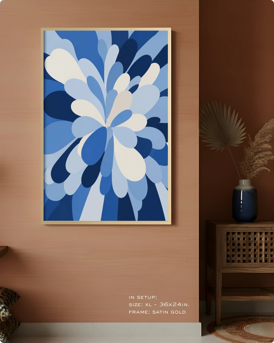 A framed abstract floral artwork in shades of blue and white hanging on a warm terracotta wall in a styled interior. The frame is satin gold.
