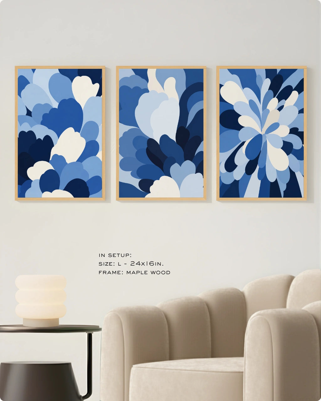 Three framed abstract blue floral wall art prints displayed above a beige sofa in a modern living room setting. The prints feature layered organic shapes in shades of blue, navy, and white, enclosed in light natural wood frames.