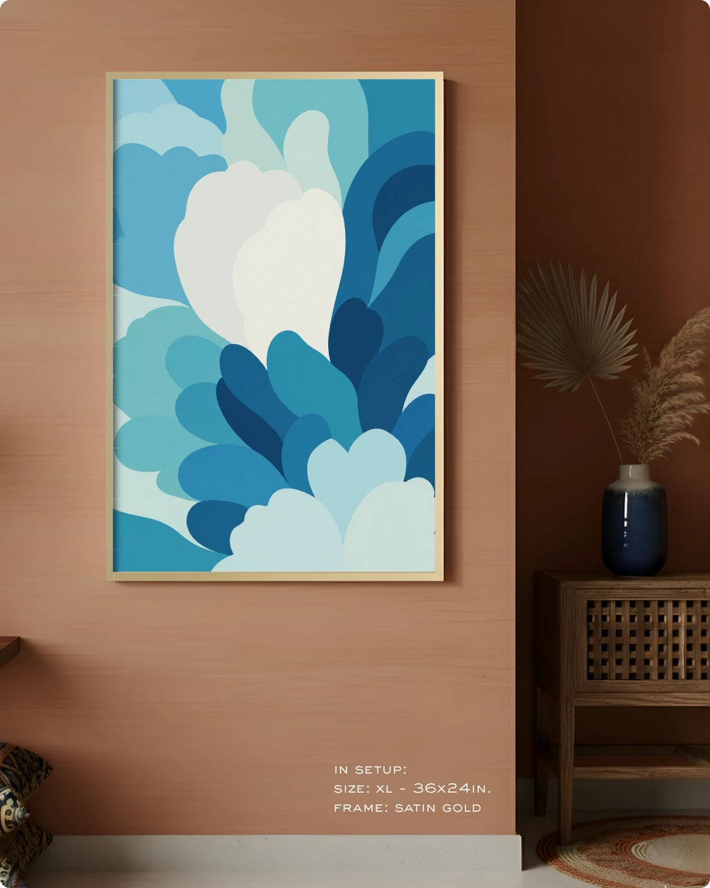 A framed abstract art print featuring layered blue and white cloud-like shapes, displayed on a warm terracotta wall in a styled interior setting with a side table and vase.