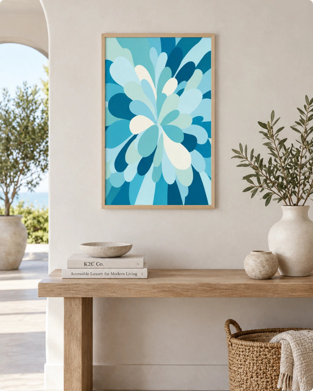 A framed abstract floral art print in shades of blue and white hangs on a beige wall above a wooden console table styled with vases, books, and a basket.