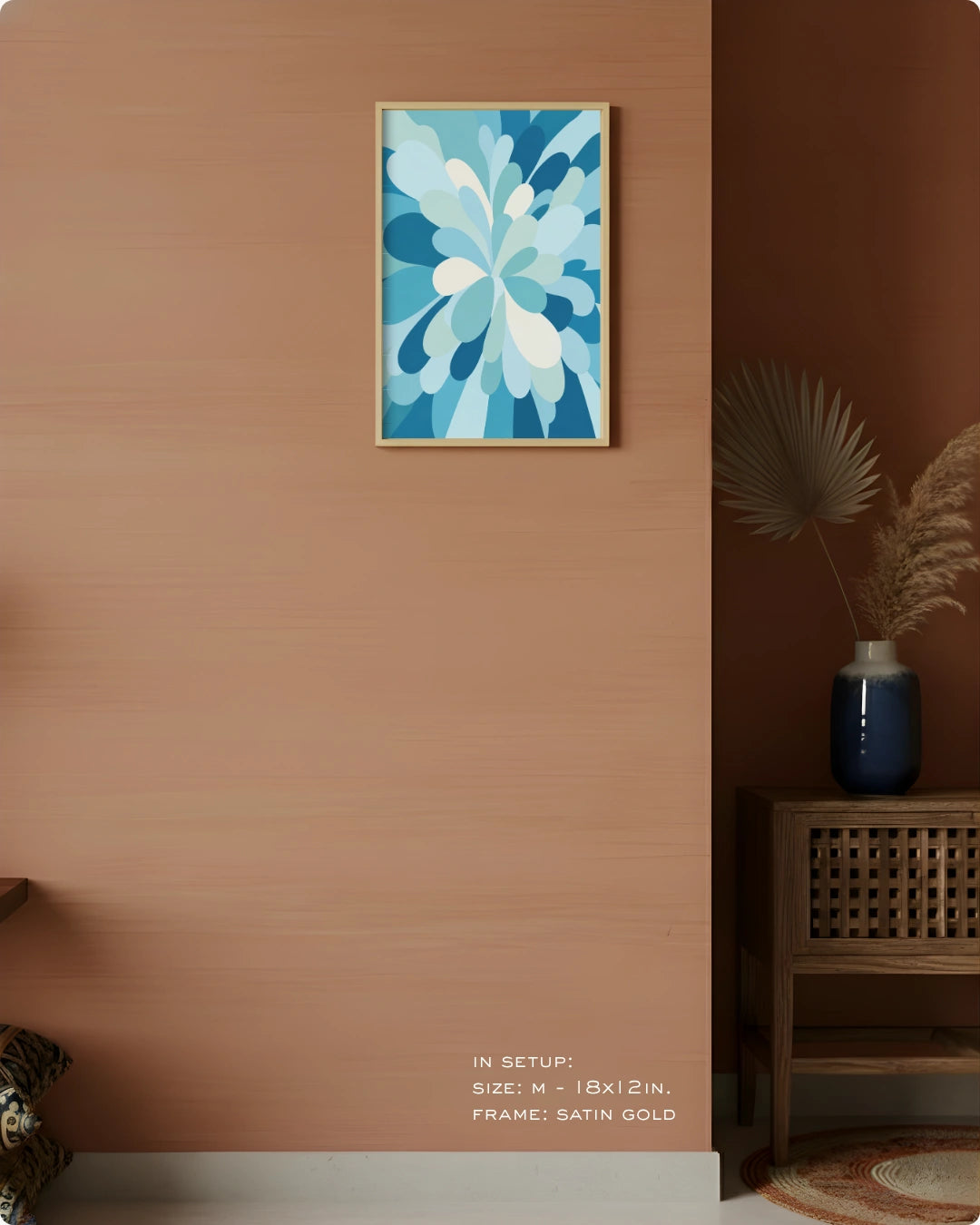 A framed abstract floral art print in shades of blue and white with a satin gold frame, displayed on a warm terracotta wall in a styled interior setting.