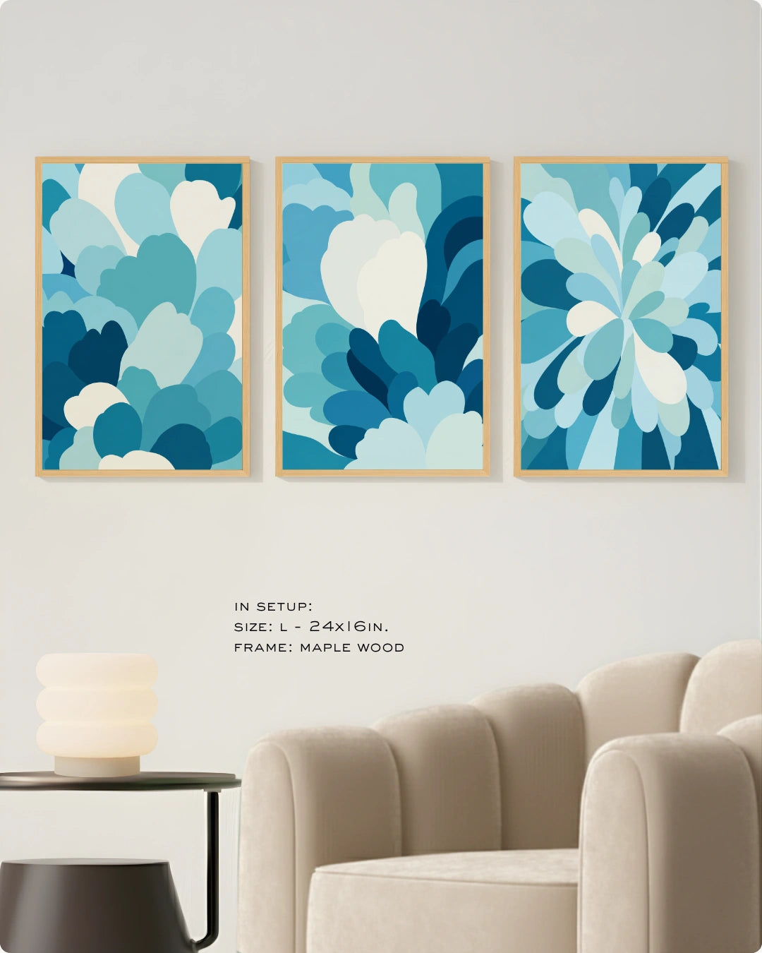 Three framed abstract blue floral wall art prints displayed above a beige sofa in a modern living room setting. The prints feature layered organic shapes in shades of blue, teal, and white, enclosed in light wood frames.