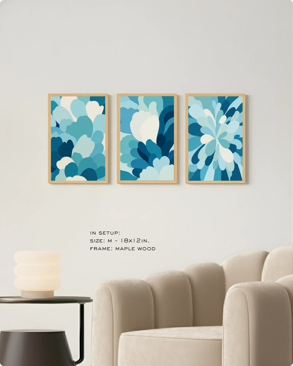 Three framed abstract floral wall art prints in shades of blue and white, displayed side-by-side on a light gray wall above a beige armchair and small side table.