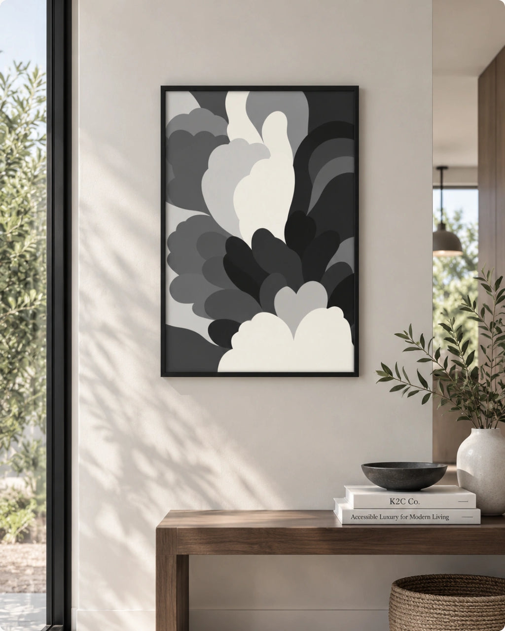 A framed abstract wall art print with layered cloud-like shapes in black, gray, and white, displayed on a beige wall above a wooden console table in a modern interior setting.