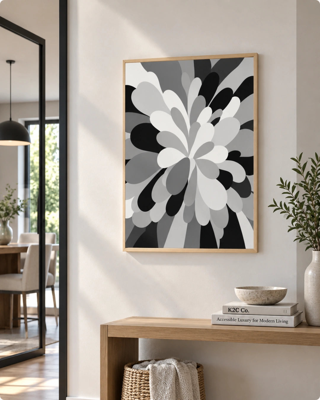 A framed abstract floral wall art print with black, gray, and white organic shapes hangs on a light beige wall above a wooden console table in a modern interior setting.