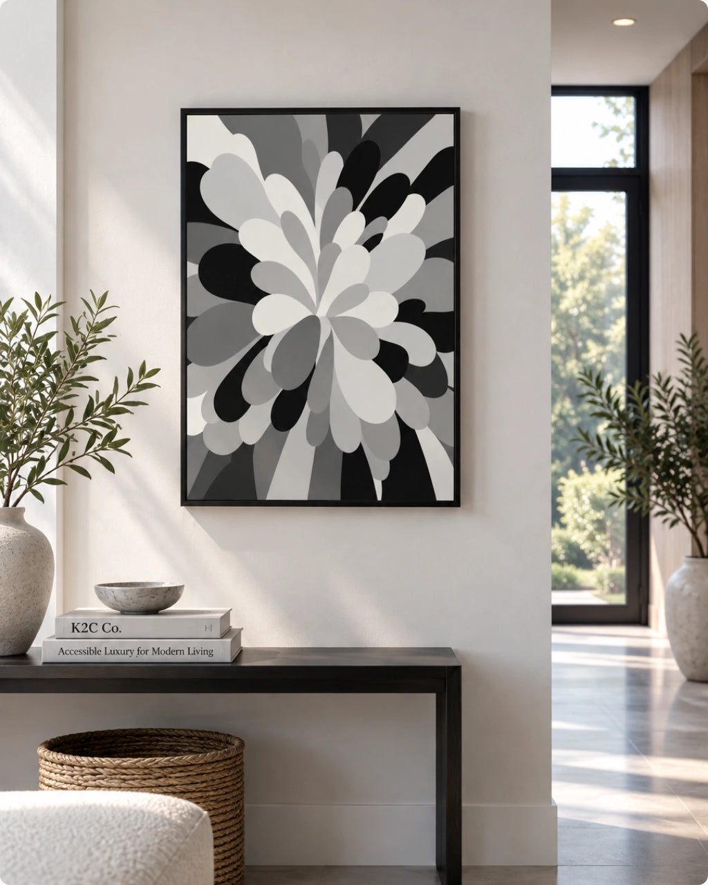A framed abstract floral art print in black, white, and gray hangs on a light beige wall above a dark console table in a modern, sunlit interior.