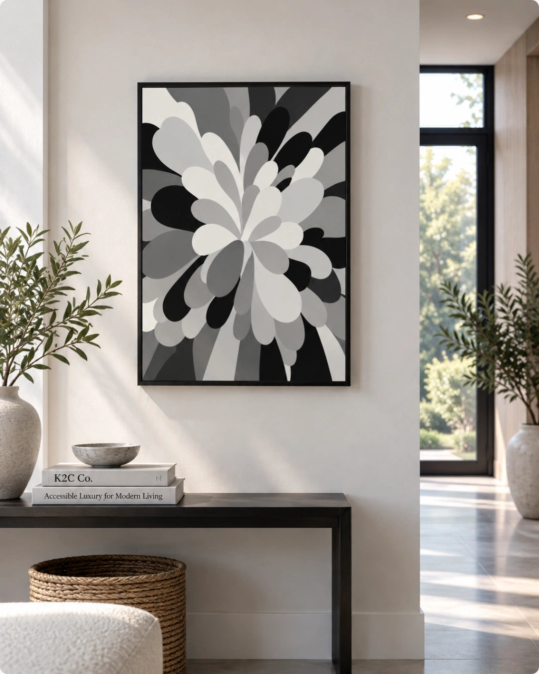 A framed abstract floral art print in black, white, and gray hangs on a light beige wall above a dark console table in a modern, sunlit interior.