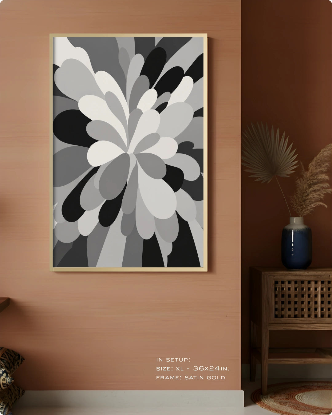 A framed abstract floral wall art print in grayscale hangs on a warm terracotta wall in a styled interior. The artwork features layered petal-like shapes in white, gray, black, and charcoal tones, enclosed in a thin gold frame.