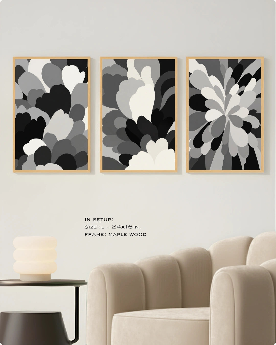 Three framed abstract floral wall art prints in black, gray, and white are displayed above a beige armchair in a modern living room setting. The frames are light wood.