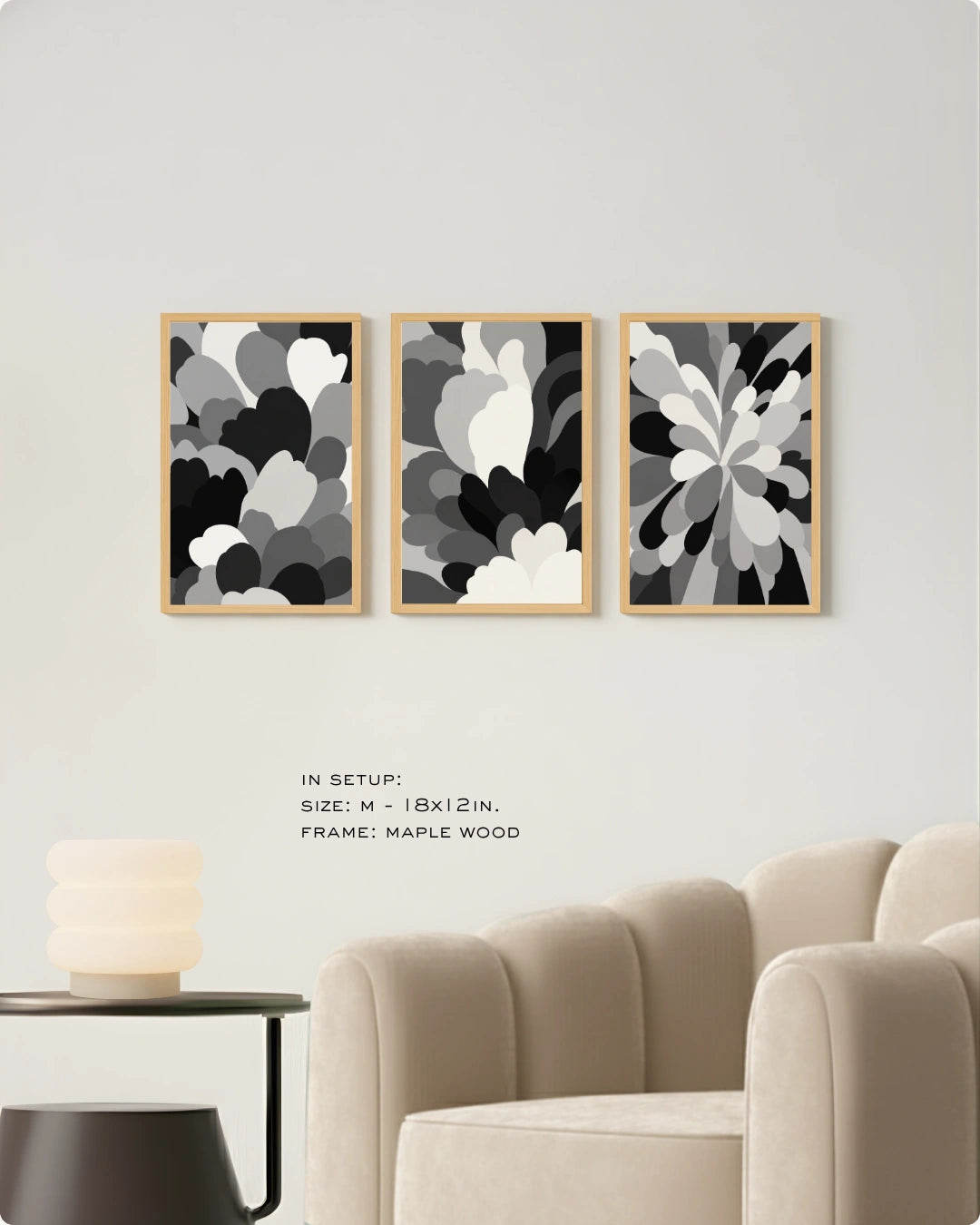 Three framed abstract floral wall art prints in black, gray, and white are displayed on a light gray wall above a beige armchair, with small text noting size and maple wood frames.