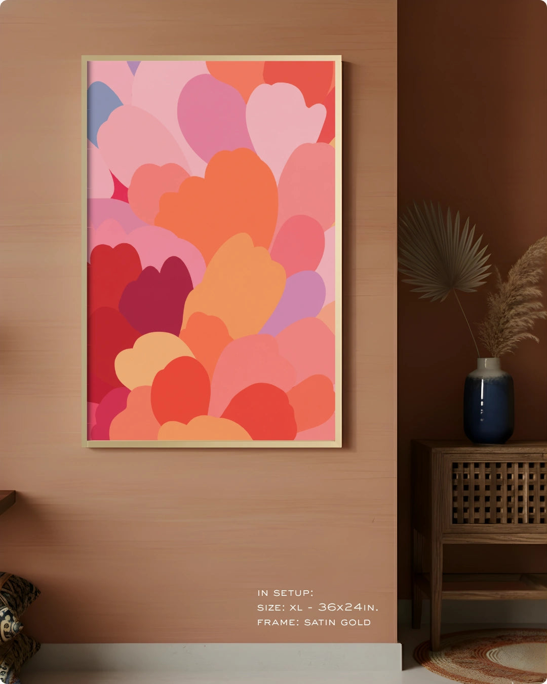 A framed abstract wall art print with overlapping heart-like shapes in pink, coral, orange, red, and purple tones, displayed on a warm beige wall in a styled interior setting with a side table and vase.