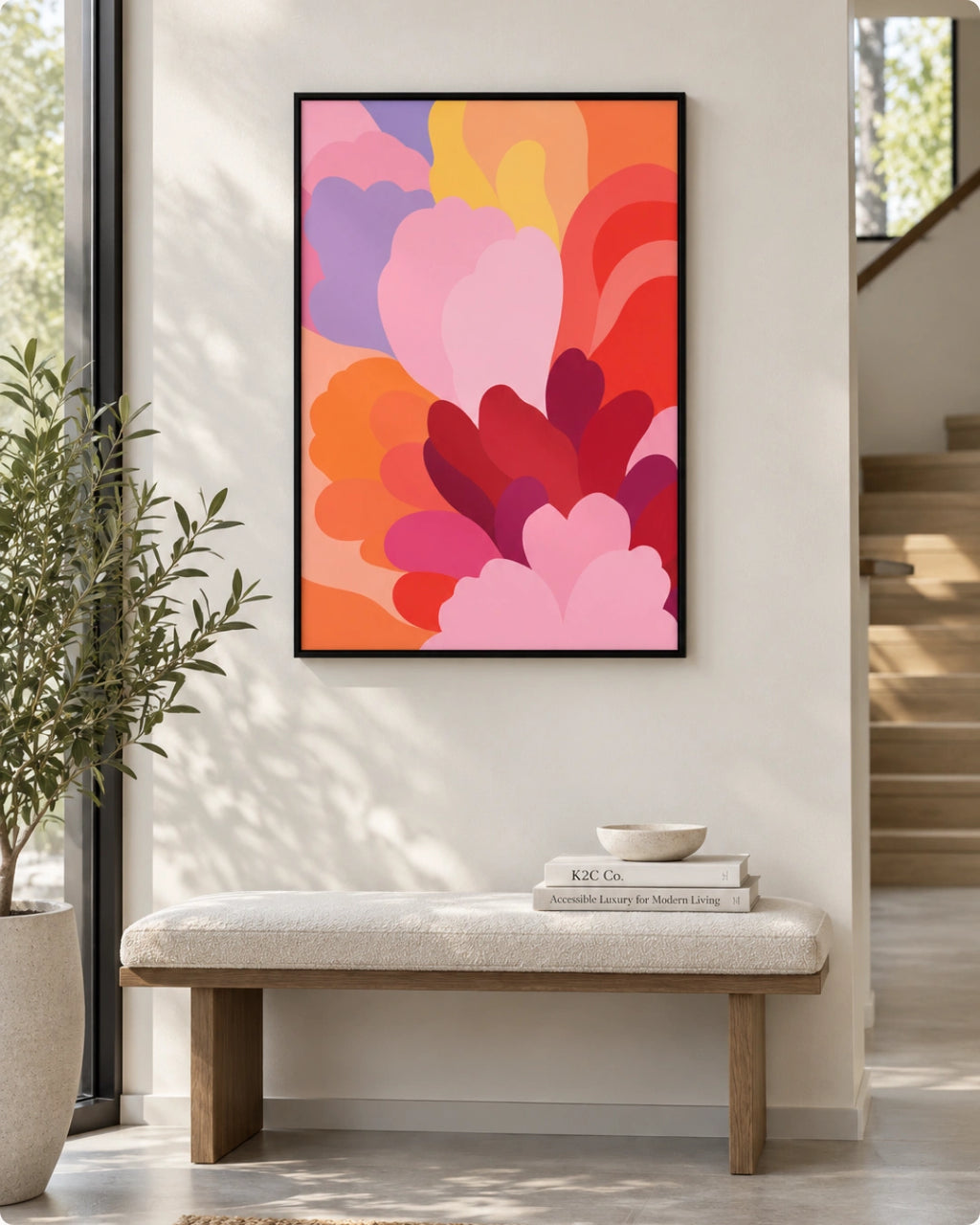 A framed abstract floral art print with layered pink, red, orange, purple, and yellow petals hanging on a light beige wall above a white bench in a modern entryway.