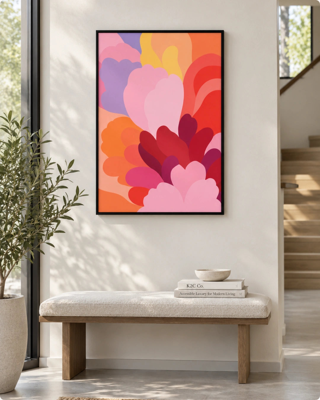 A framed abstract floral art print with layered pink, red, orange, purple, and yellow petals hanging on a light beige wall above a white bench in a modern entryway.