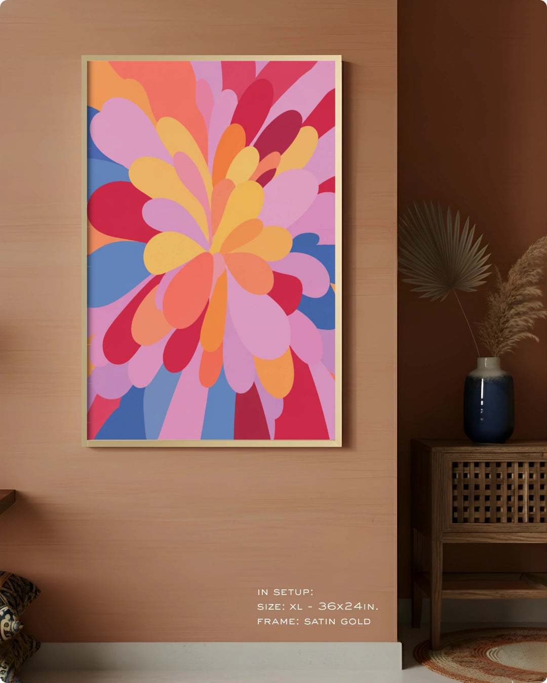 A framed abstract floral wall art print hangs on a warm wood-paneled wall in a styled interior. The artwork features layered petal-like shapes in pink, orange, yellow, red, and blue, with a thin gold frame.