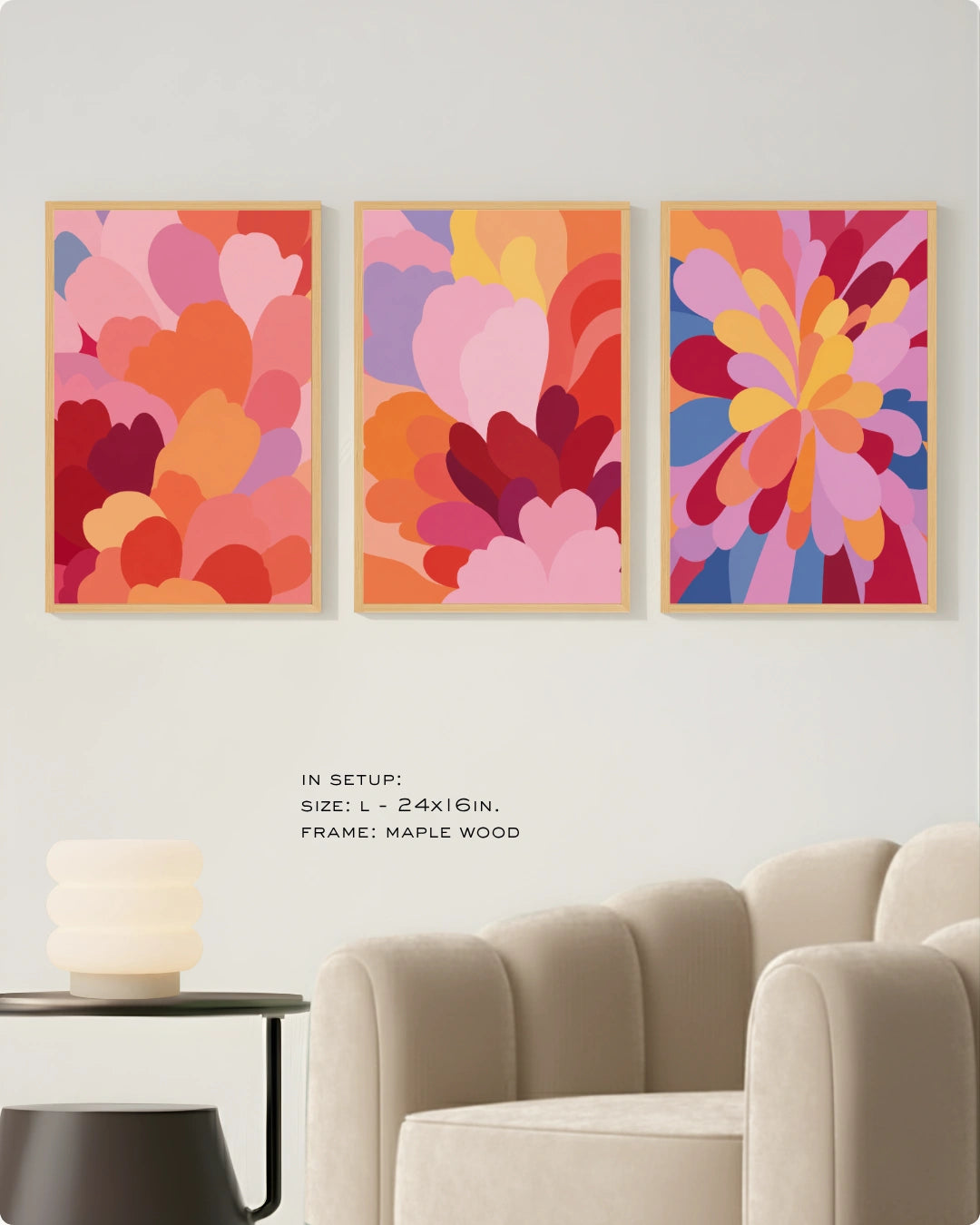 Three framed abstract floral wall art prints in warm pink, orange, red, yellow, and purple tones, displayed above a cream sofa in a modern living room setting. Small text below reads: 'IN SETUP: SIZE: L - 24x16in.
