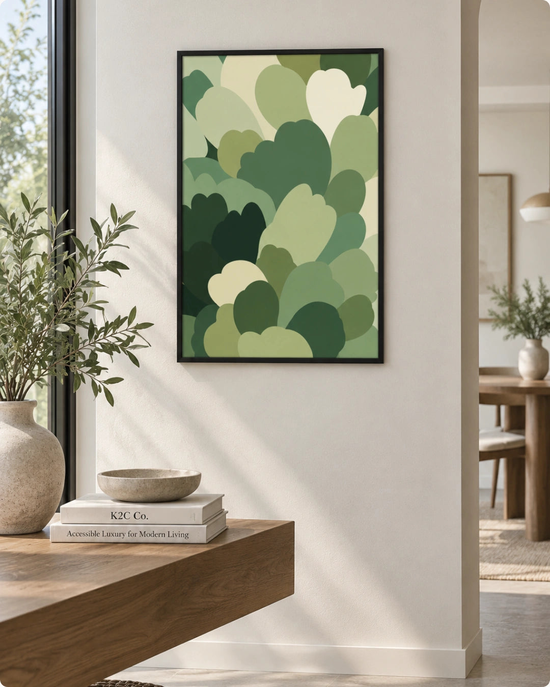 A framed wall art print featuring an abstract pattern of layered green and cream leaf-like shapes, displayed in a modern interior setting on a light beige wall above a wooden console table.