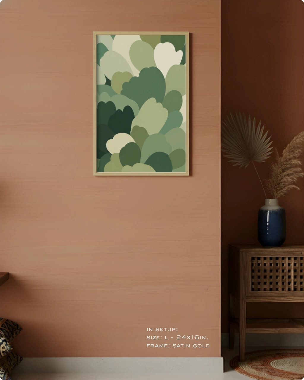 A framed wall art print featuring layered abstract heart-like shapes in shades of green and cream, displayed on a warm terracotta wall in a styled interior setting with a side table, blue vase, and dried palm leaves.