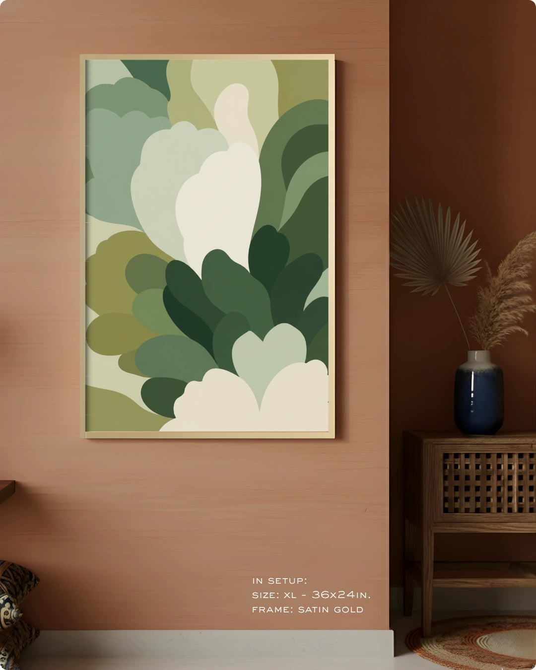 A framed abstract botanical art print with layered green and cream leaf-like shapes, displayed on a warm terracotta wall in a styled interior setting with a side table and vase.