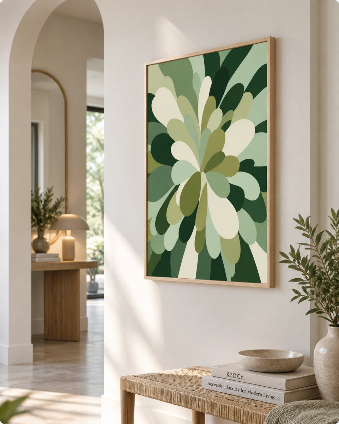 A framed abstract botanical art print with layered green and cream leaf-like shapes hanging on a warm beige wall in a styled interior hallway with a bench, books, and plants.