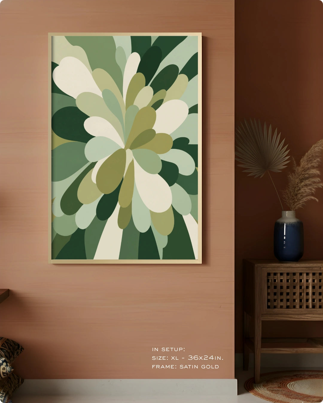 A framed abstract botanical art print with layered green and cream petal-like shapes, displayed on a warm terracotta wall in a styled interior setting with a side table and vase.