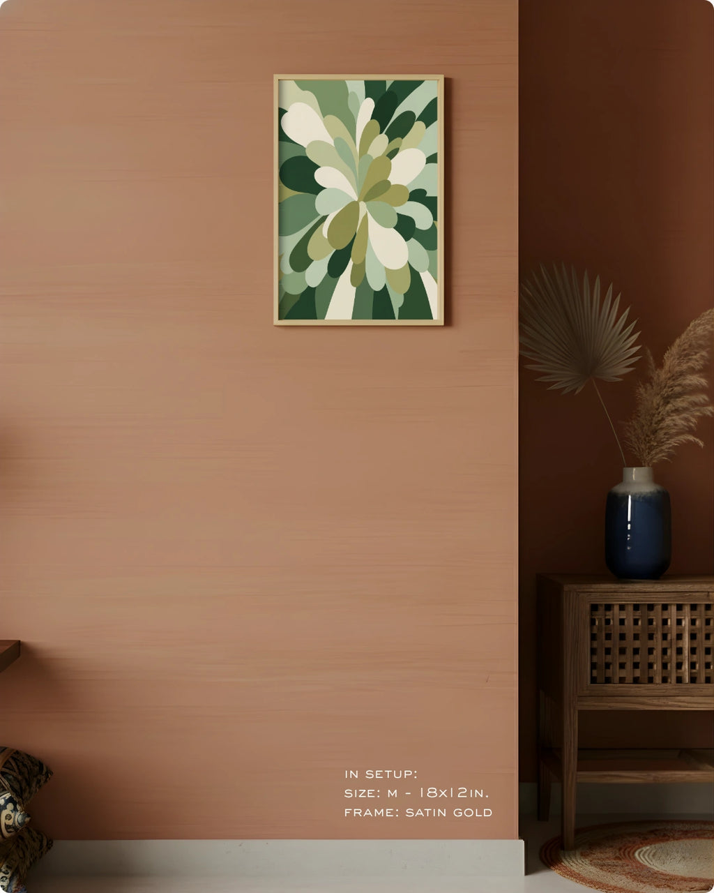 A framed abstract floral wall art print hangs on a warm terracotta-colored wall in a styled interior. The artwork features layered green, olive, and cream leaf-like shapes with a thin satin gold frame.
