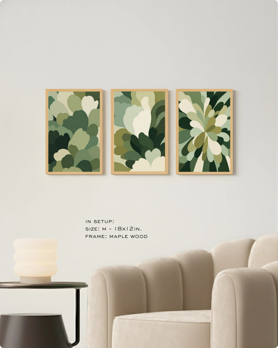 Three framed abstract floral wall art prints in shades of green and cream hang on a light gray wall above a beige armchair, with small text below reading 'IN SETUP: SIZE: M - 18x12 IN. FRAME: MAPLE WOOD'.
