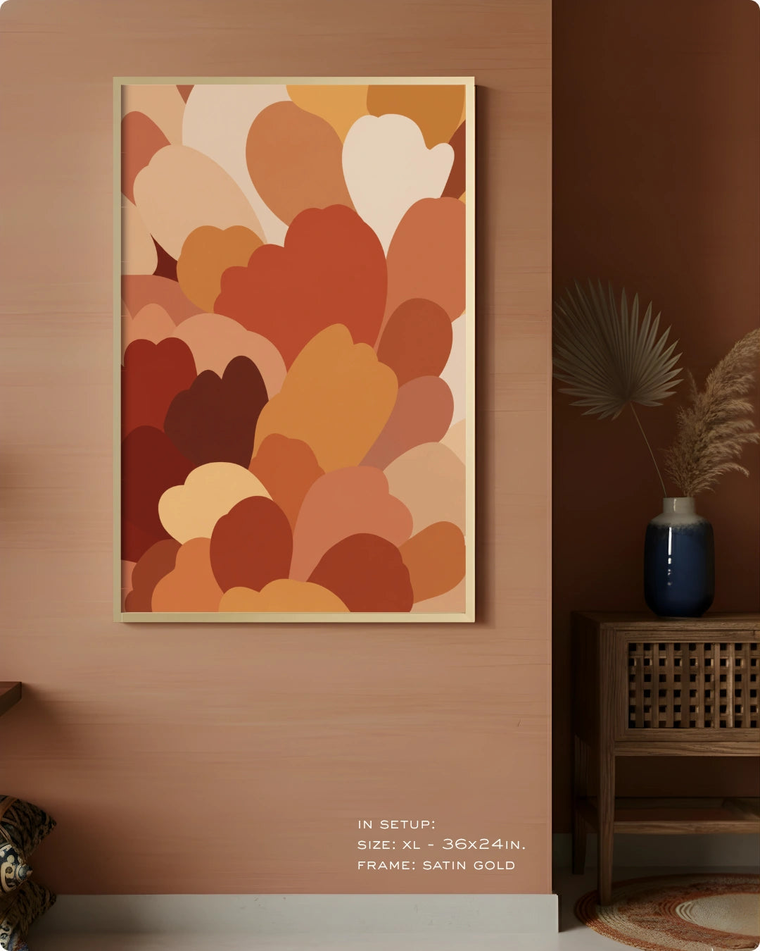 A framed abstract wall art print hangs on a warm peach-brown wall in a styled interior. The artwork features layered organic heart-like shapes in terracotta, rust, orange, tan, cream, and brown tones.