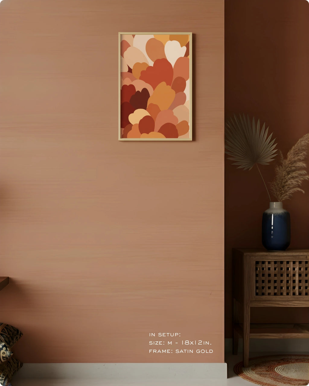 A framed abstract art print with overlapping organic shapes in warm tones of orange, rust, beige, and cream, displayed on a textured terracotta wall in a styled interior setting.