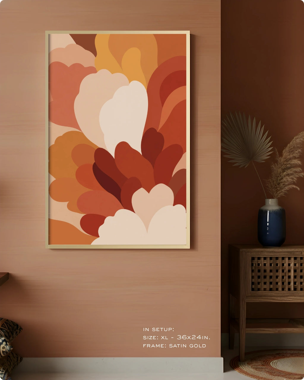 A framed abstract wall art print with layered organic shapes in warm orange, rust, cream, and brown tones, displayed on a peach wall in a styled interior setting with a side table and vase.